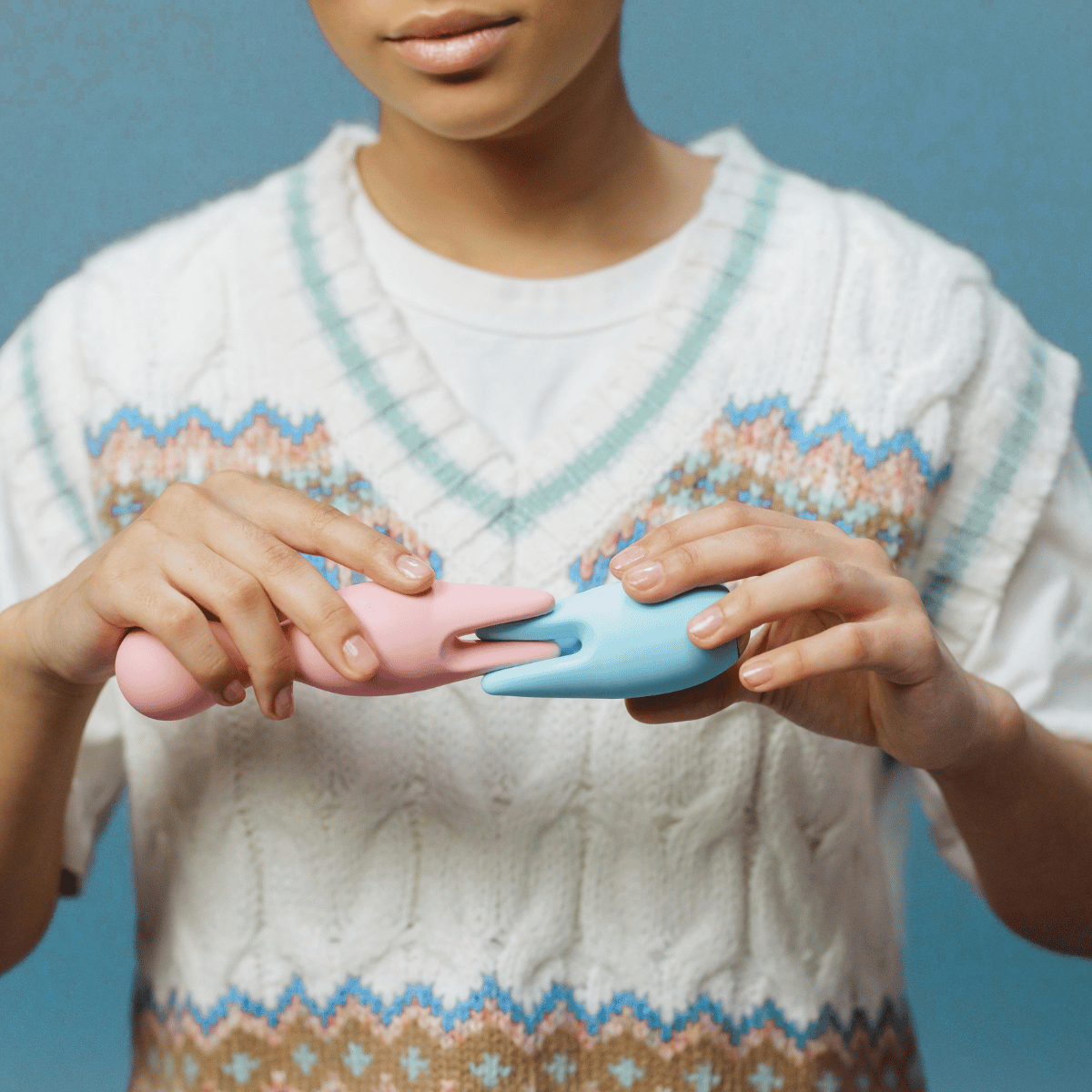 Person wearing a white sweater with patterned hem, holding two small pink and blue  female vibrator. Your Blissful Holidays.Belle Exotics holiday sale – sensual gifts, couples toys, and self-care essentials. Private delivery nationwide.