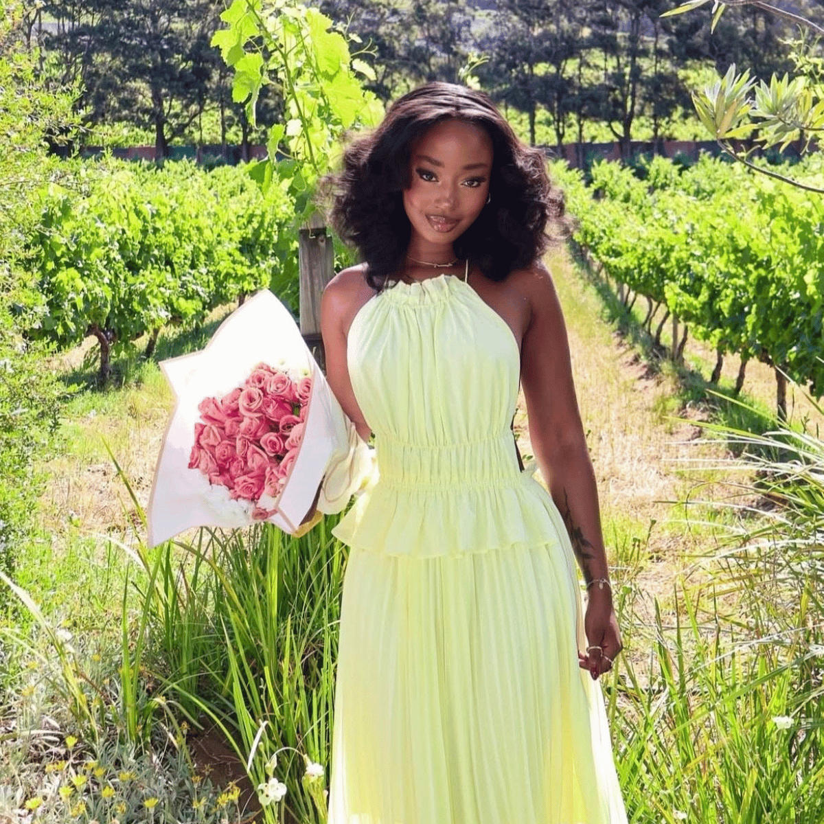 Woman in a yellow dress holding pink flowers in a vineyard..Here’s to More
More pleasure. More confidence. More exploration. More Belle.6 years of pleasure toys with Belle Exotics Toys Trinidad and Tobago
