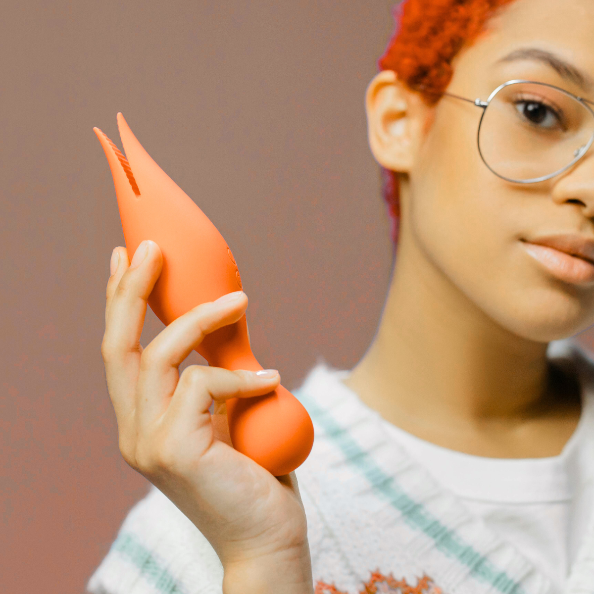 Person holding an orange VIBRATOR Against a brown background.Discover Pleasure & Sensuality at Belle Exotics. Elevate intimacy with our luxury collection of pleasure products. Shop online or visit our Trinidad store for an extraordinary experience. Ignite your senses today.