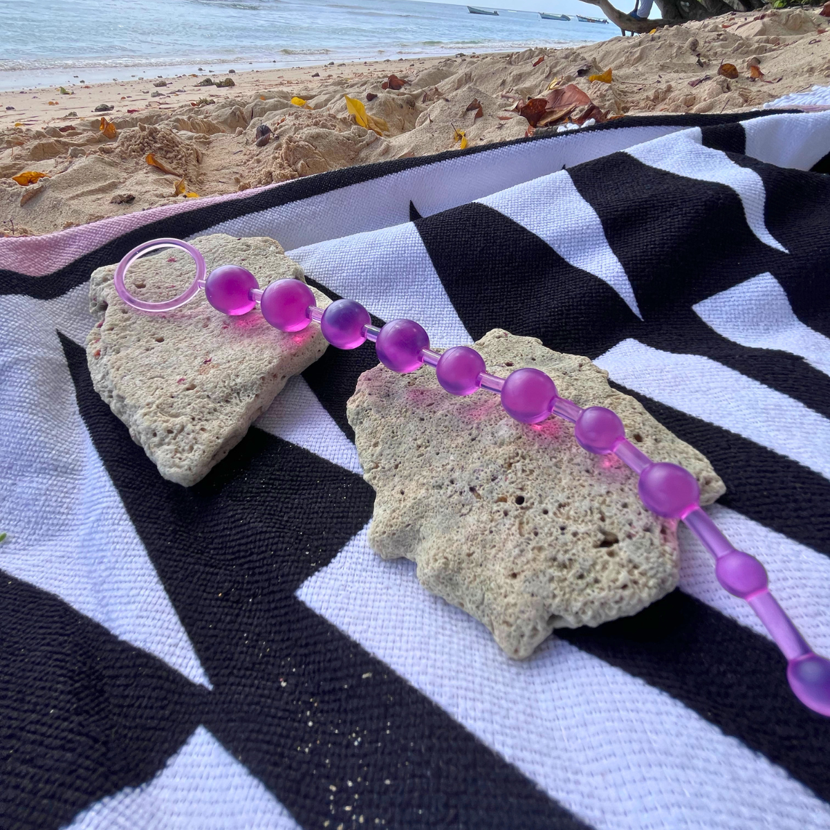 A purple translucent beaded personal massager with a ring attachment, laid out on a black and white striped beach towel on the sand with the ocean in the background.Belle Exotics is a discreet adult toy and sexual wellness store in Trinidad and Tobago, offering pleasure products, lubricants, lingerie, couple toys, self-love essentials, and intimacy accessories for private online and in-store shopping.   Belle Exotics offers discreet adult toys, lubricants, lingerie, and sexual wellness products in Trinidad 