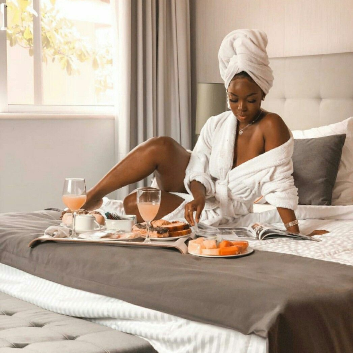 Woman in a robe sitting on a bed with a tray of food and drinks.    Discover pleasure products in Trinidad and Tobago from Belle Exotics, including couple toys, lubricants, lingerie, and beginner-friendly adult products.