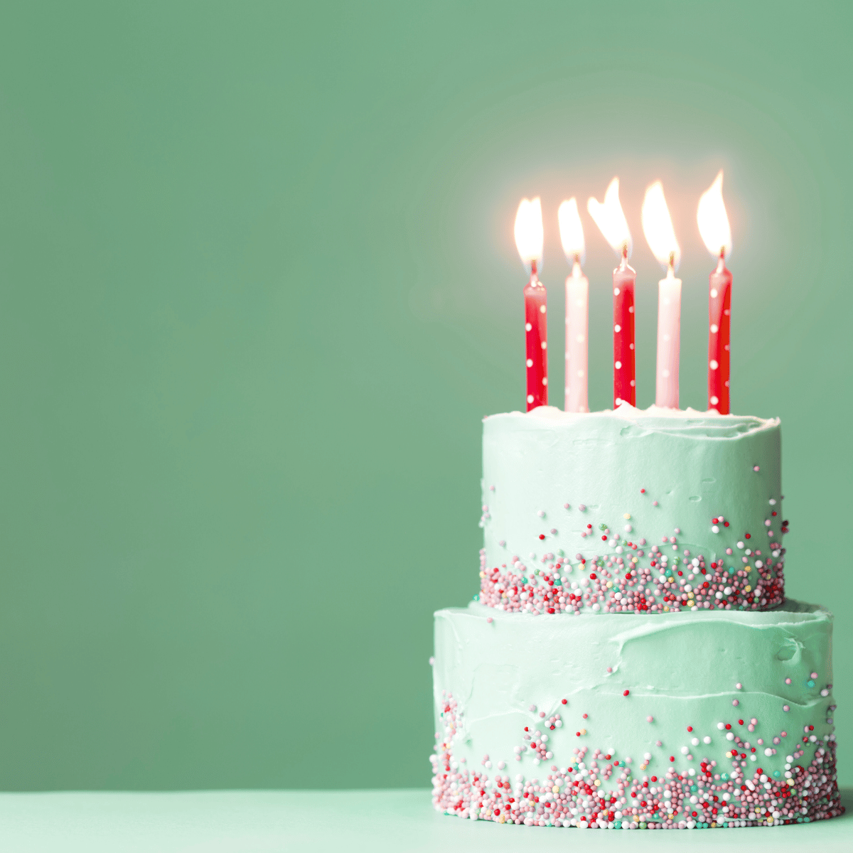 Two-tiered birthday cake with lit candles on a green background.After 6 years, Belle Exotics isn’t just a brand—it’s a journey customers continue to grow in.