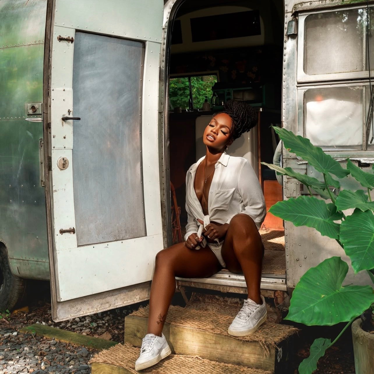 Woman sitting inside a vintage trailer with plants around.    Discover pleasure products in Trinidad and Tobago from Belle Exotics, including couple toys, lubricants, lingerie, and beginner-friendly adult products.