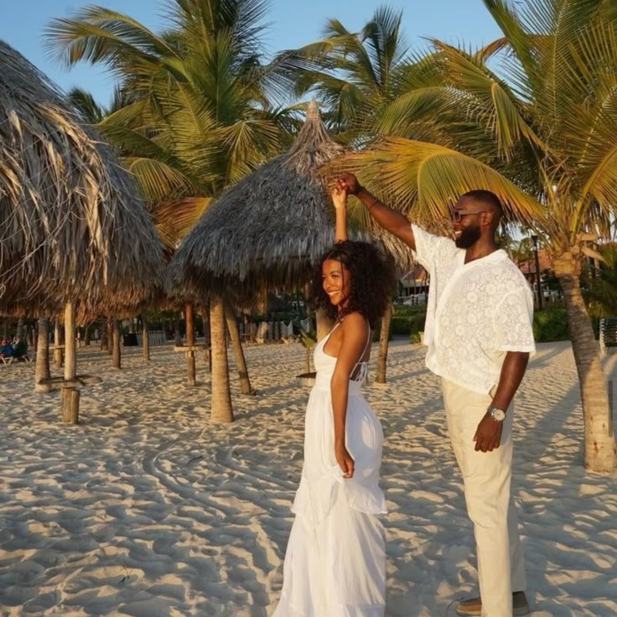 Couple in white on a beach with palm trees and thatched huts. Shop adult toys in Trinidad and Tobago at Belle Exotics, with solo toys, couple products, self-love essentials, and discreet delivery options.