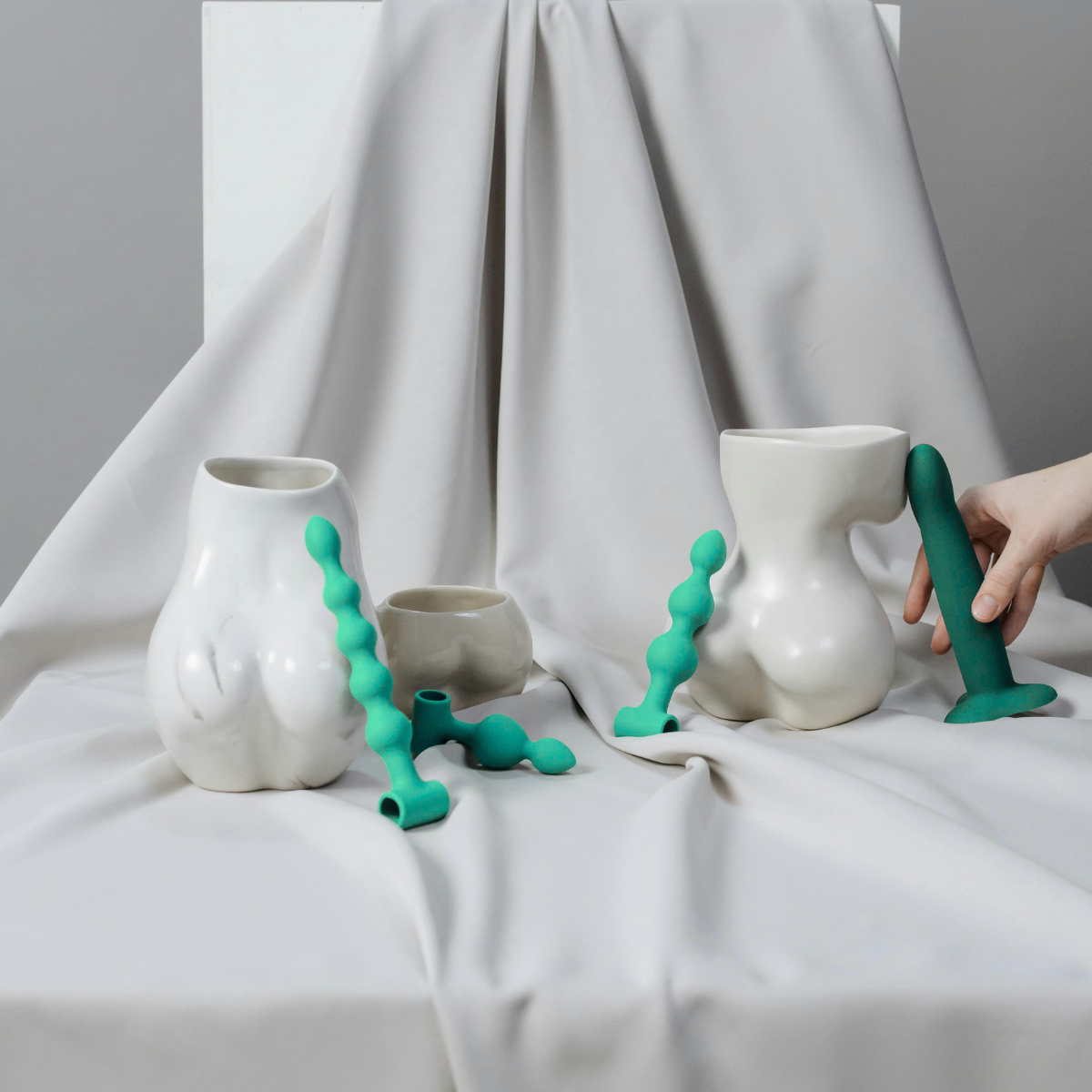White vases with green female vibrators elements on a white fabric background.Your Golden Hour campaign by Belle Exotics in Trinidad and Tobago promoting confident exploration, sexual wellness, and guided intimacy in-store and online.