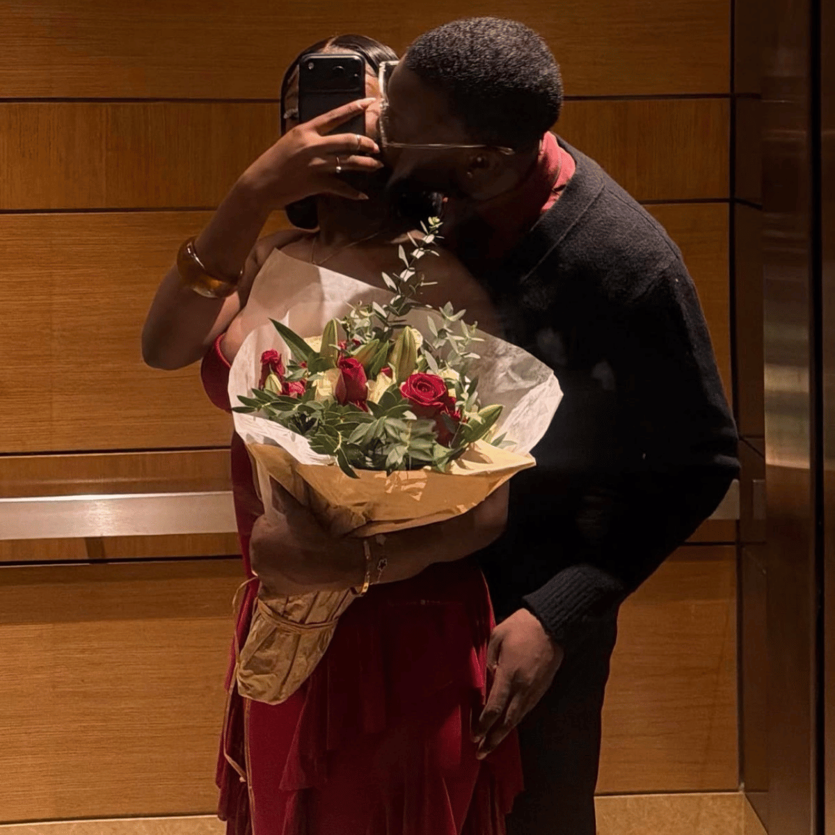 A couple shares a kiss in a mirror selfie inside what appears to be a hotel lobby or elevator. The woman is wearing a deep red dress and holding a gold handbag while holding a bouquet of red roses wrapped in beige paper.Belle Exotics is a discreet adult toy and sexual wellness store in Trinidad and Tobago, offering pleasure products, lubricants, lingerie, couple toys, self-love essentials, and intimacy accessories for private online and in-store shopping.   Belle Exotics offers discreet adult toys.