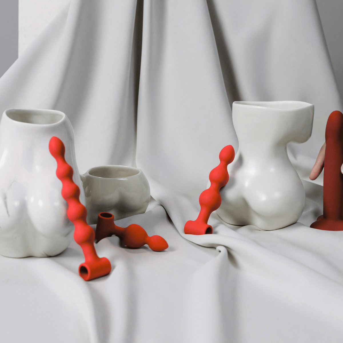 A set of anal plugs ceramic vases and abstract red silicone wavy accessories arranged on draped white fabric.Shop Belle Exotics for intimacy, pleasure and adult wellness products in Trinidad & Tobago. Shop online or visit our Marabella and Valsayn locations.