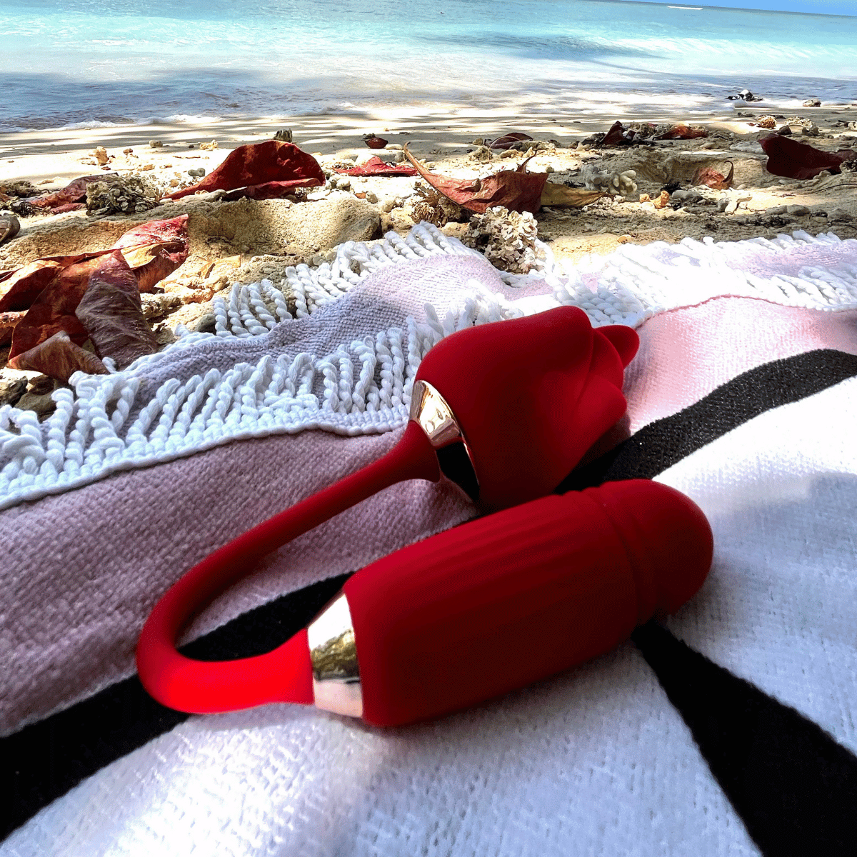 A red handheld personal massager with metallic silver accents rests on a white, pink, and black patterned blanket on a beach, with sand, shells, and turquoise water in the background.Belle Exotics is a discreet adult toy and sexual wellness store in Trinidad and Tobago, offering pleasure products, lubricants, lingerie, couple toys, self-love essentials, and intimacy accessories for private online and in-store shopping.   Belle Exotics offers discreet adult toys.