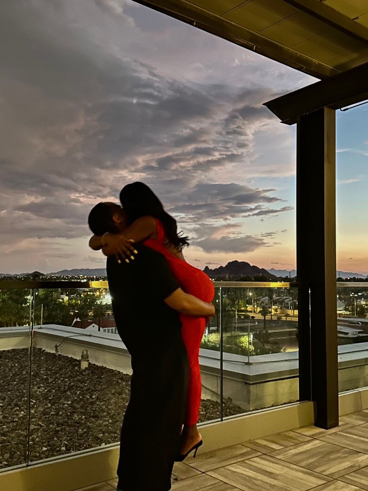 Two people embracing on a rooftop with a cityscape and sunset in the .Hand holding a transparent vibrator object with red interior on a light pink background.Discover Belle Exotics, your destination for luxury adult toys and wellness products. Shop discreetly in Trinidad and Tobago with fast, private delivery. Elevate intimacy today.background